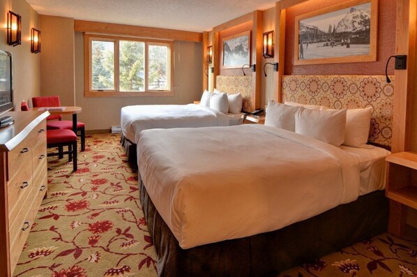 A hotel room with two beds, a desk, a chair, and a television.