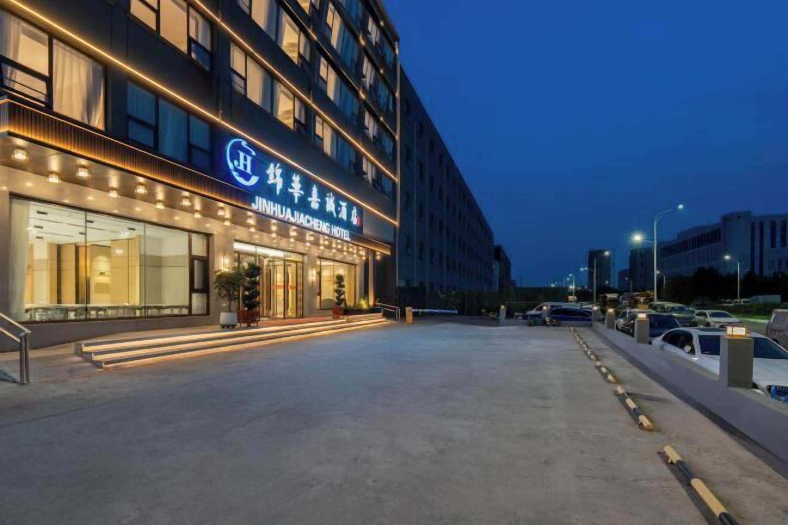 Ein Hotel mit moderner Fassade, beleuchteter Beschilderung und einem Parkplatz mit Autos.