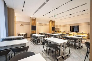 Une salle de conférence moderne, équipée de tables et de chaises, d’un grand écran et d’un coin cuisine.