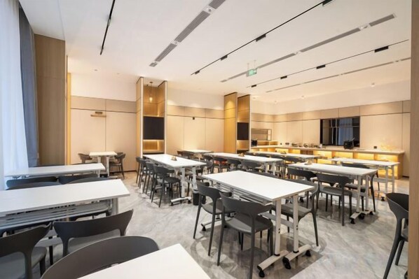 Une salle de conférence moderne, équipée de tables et de chaises, d’un grand écran et d’un coin cuisine.
