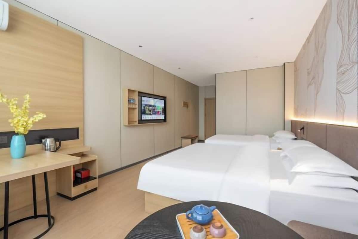 A hotel room with a bed, a desk with a vase, a television, and a wall-mounted shelf.