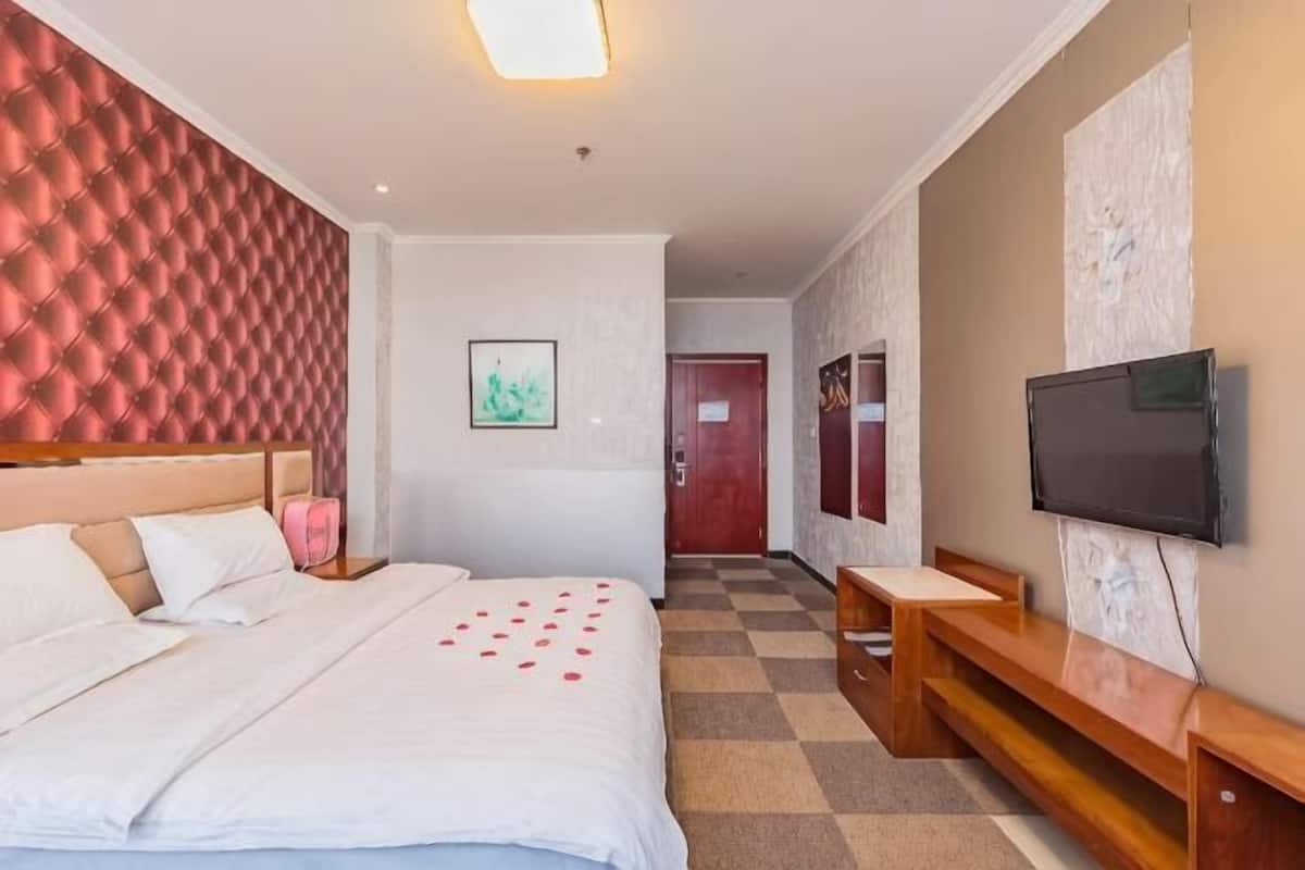 A hotel room with a large bed, a TV, a wooden bench, and a checkered floor.