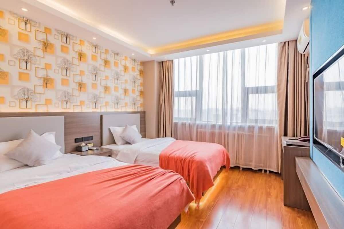 A hotel room with two beds, a large window with curtains, a wall with a geometric pattern, and a flat-screen TV.