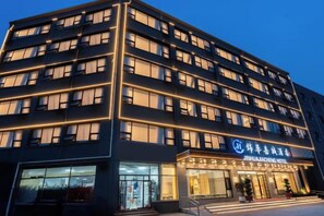 Ein mehrstöckiges Hotel mit moderner Fassade, beleuchteten Fenstern und einem gut sichtbaren Eingang mit einem Schild.