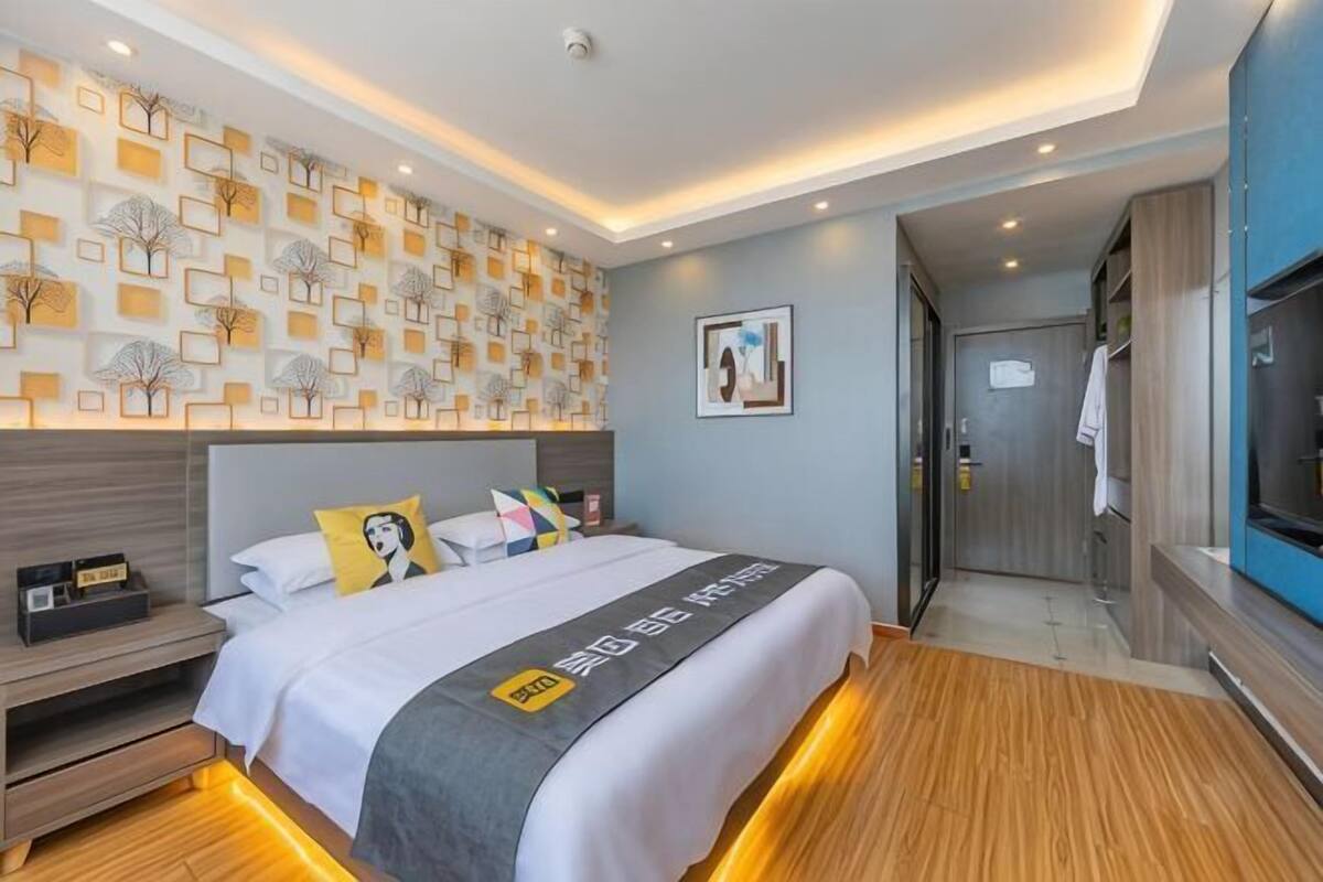 A modern hotel room with a large bed, a bedside table, a wardrobe, and a wall with a geometric pattern.