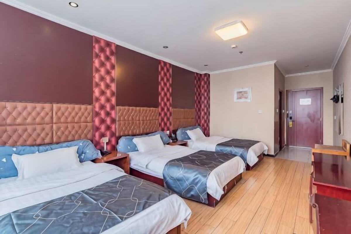 A hotel room with three beds, a wooden floor, a red accent wall, and a door in the background.