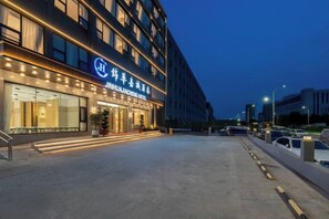 L’entrée d’un hôtel, avec une façade moderne, de grandes fenêtres et un hall d’entrée bien éclairé.