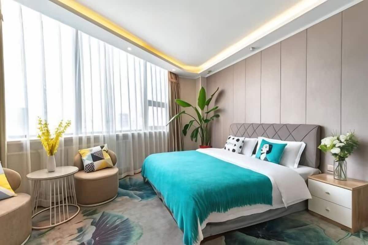 A modern hotel room with a large bed, bedside tables, a small round table, and a large window with curtains.