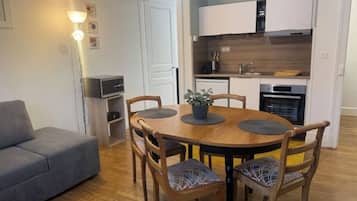 A compact living space with a dining area, kitchenette, and a gray sofa.
