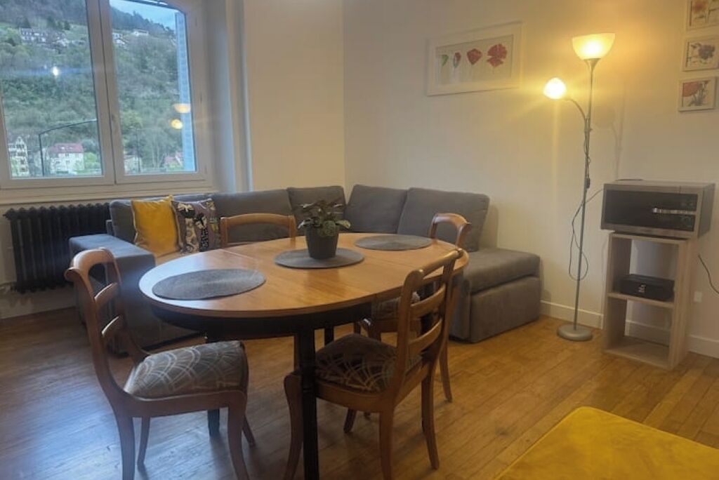 A cozy living room with a round wooden table, grey sofas, and a floor lamp.