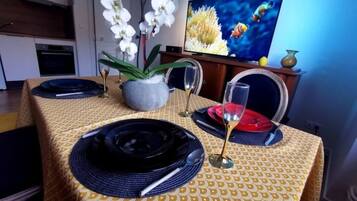 A dining table set with plates, cutlery, and a glass, with a vase of white flowers and a television in the background.