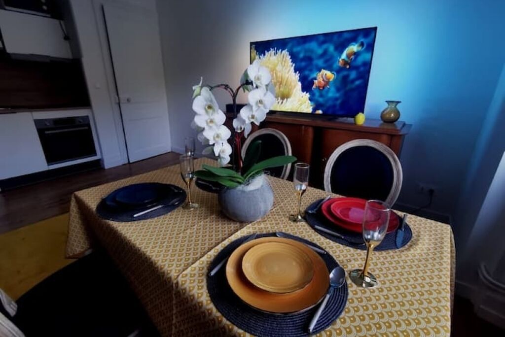 Une table à manger dressée avec des assiettes, des couverts et un vase de fleurs.