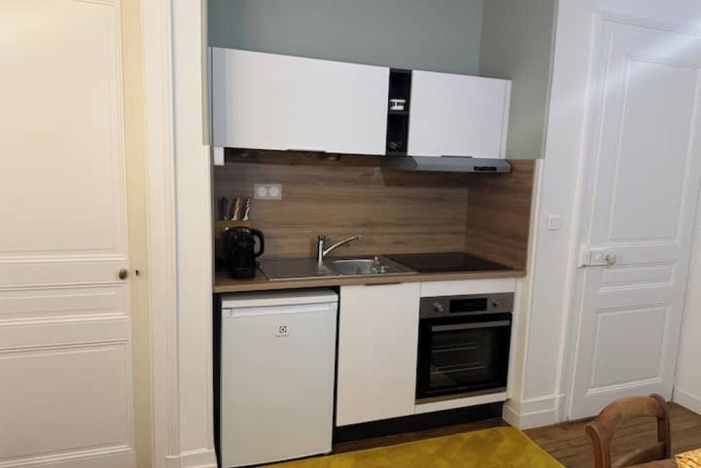 Eine kompakte Küche mit weißen Schränken, einem eingebauten Backofen und einem kleinen Kühlschrank.