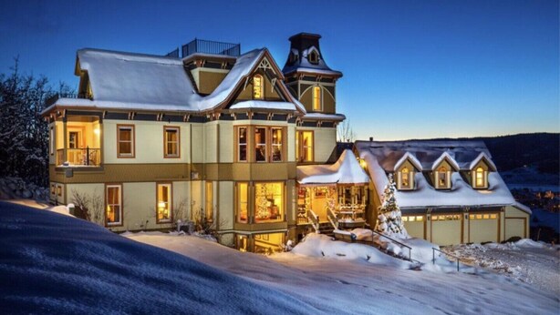 Una casa grande de varios pisos con tejado cubierto de nieve y una entrada iluminada.