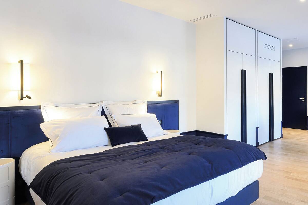 A modern bedroom with a large bed, two bedside tables, and a wardrobe.