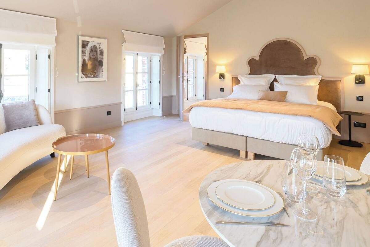 A spacious bedroom with a large bed, a sitting area with a table, and a dining setup with plates and glasses.