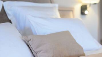 A neatly made bed with white and beige pillows, a headboard, and a wall-mounted lamp.