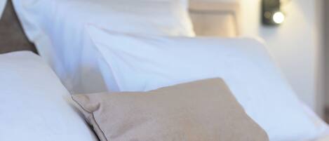 A neatly made bed with white and beige pillows, a headboard, and a wall-mounted lamp.