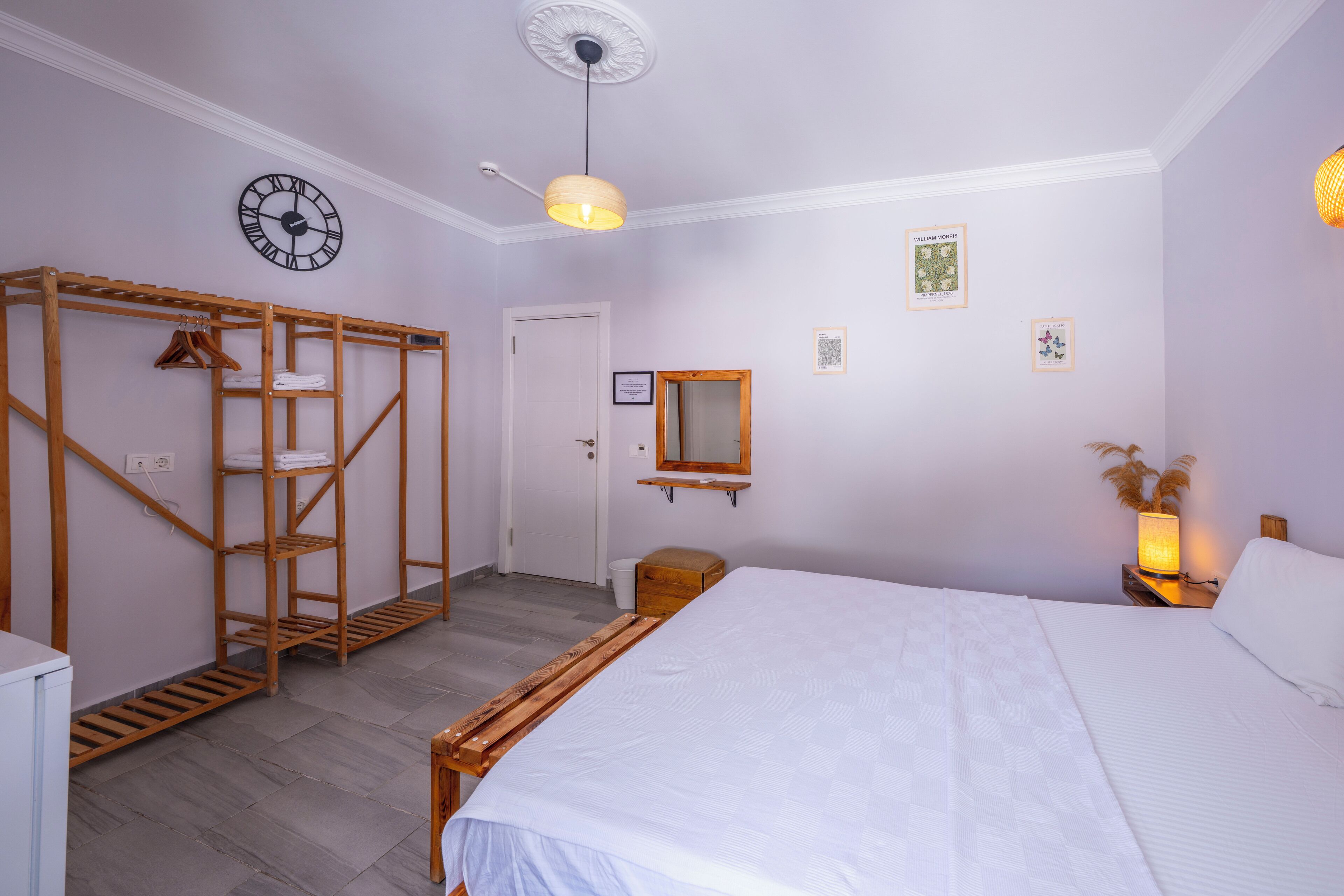 Un dormitorio con una cama, un armario de madera, un reloj, un espejo y una mesita de noche con una lámpara.