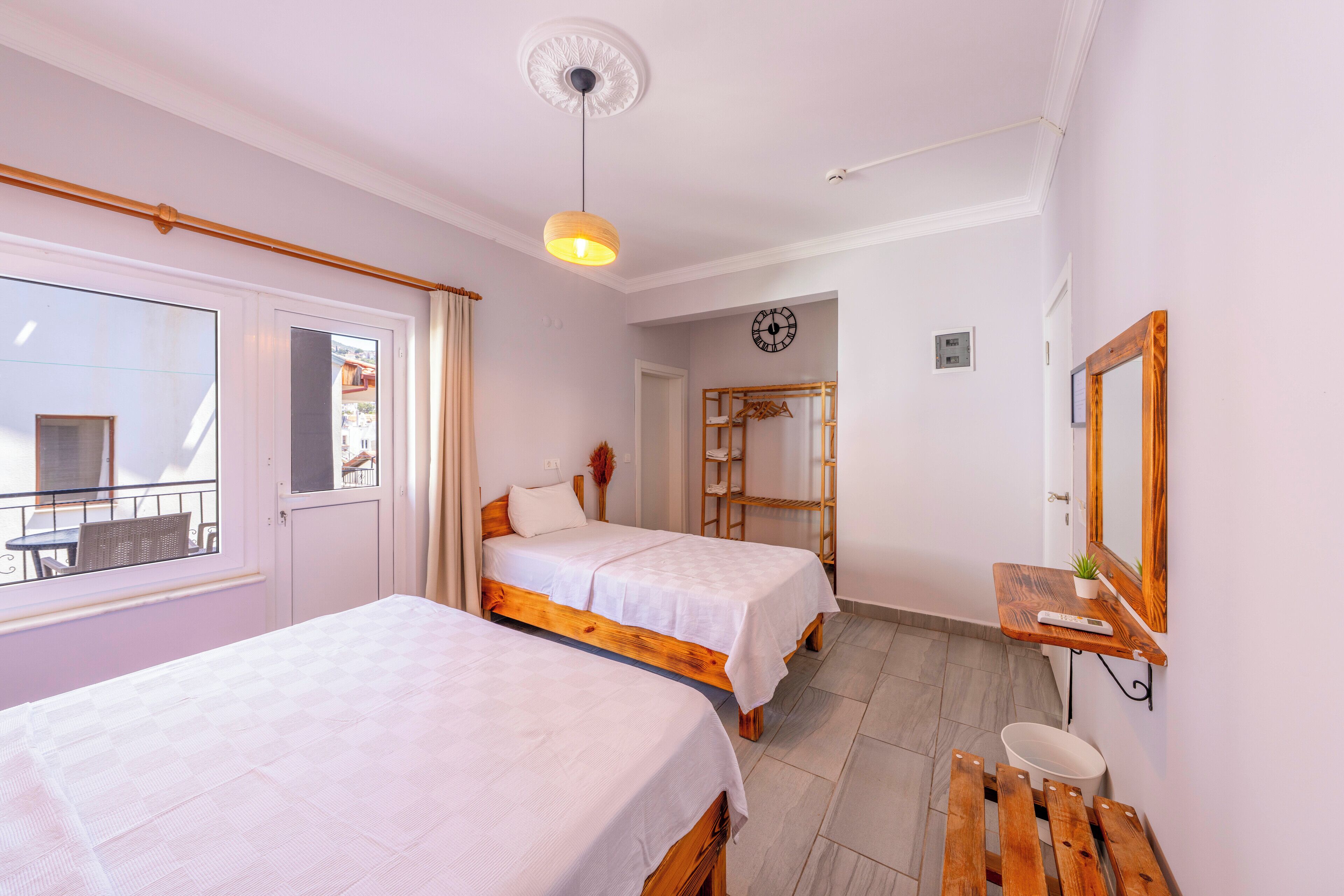 A bedroom with two beds, a small bathroom, a wooden bench, a shelf with a plant, and a window with a view.