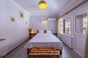 Un dormitorio con cama, mesita de noche, lámpara y ventana con vistas a edificios.