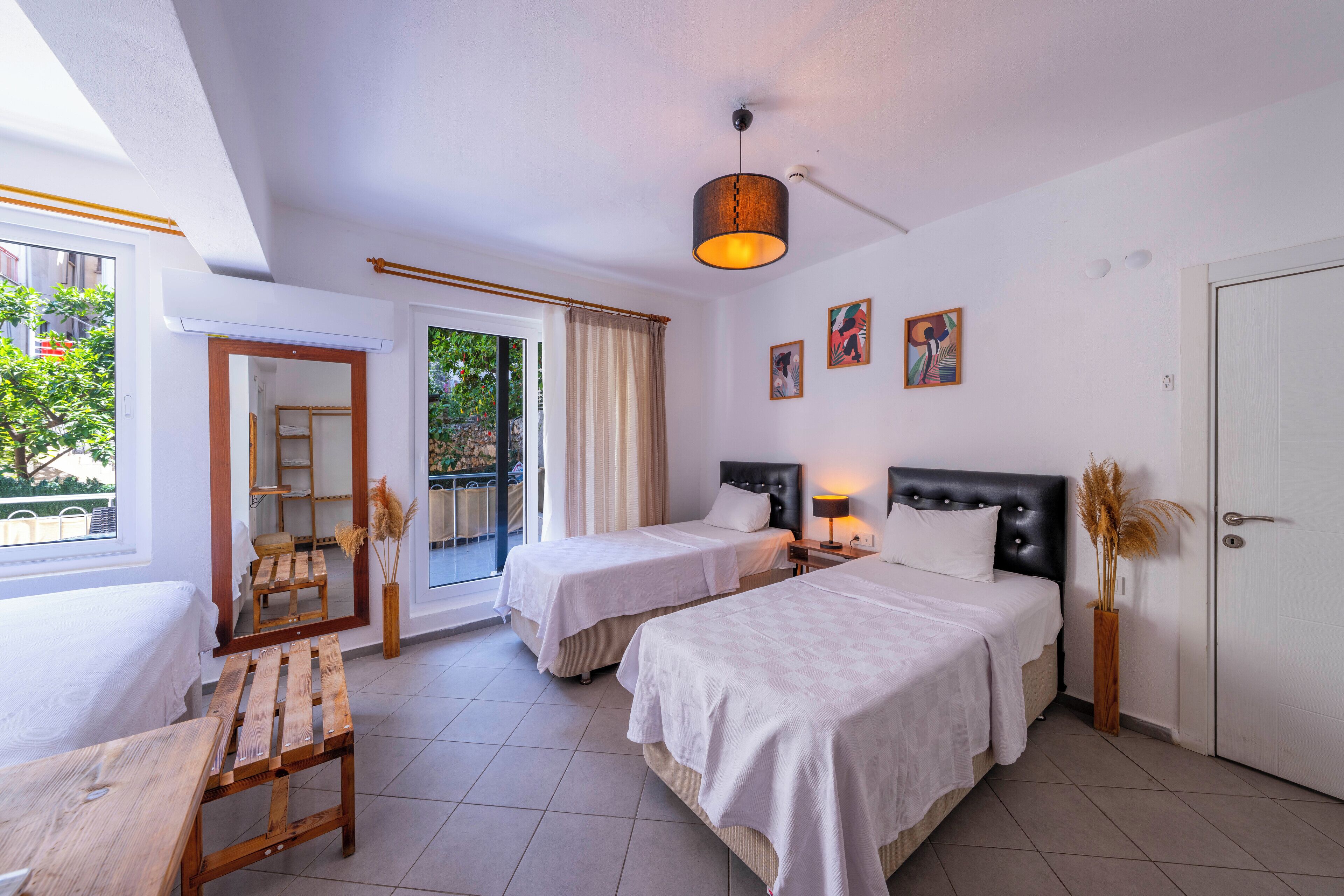 A hotel room with two beds, a wooden bench, a balcony with a view, and a door.