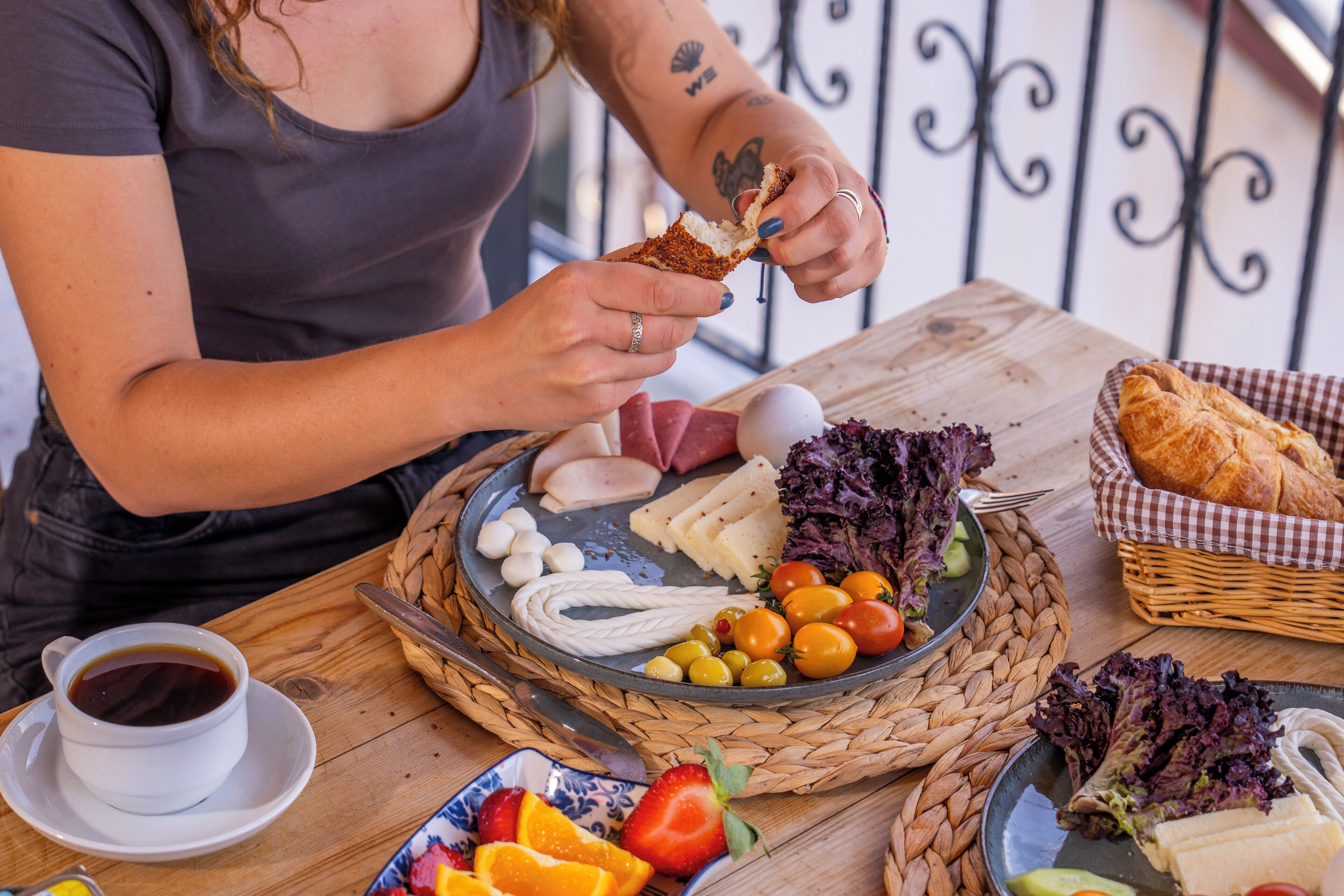 Una persona comiendo un sándwich en una mesa con diferentes alimentos y una taza de café.