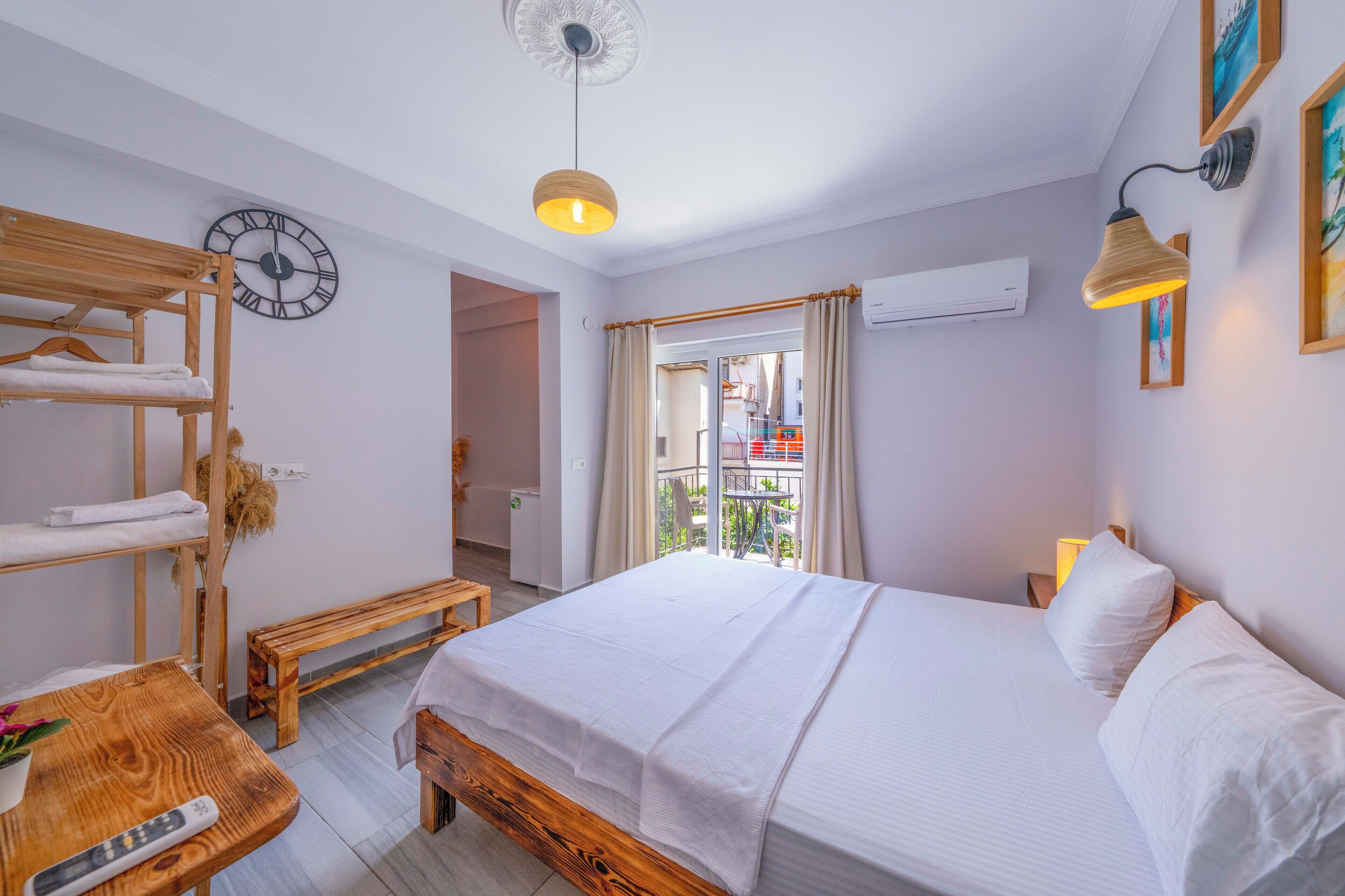 Un dormitorio con una cama, un banco de madera, un reloj de pared y una ventana con cortinas.