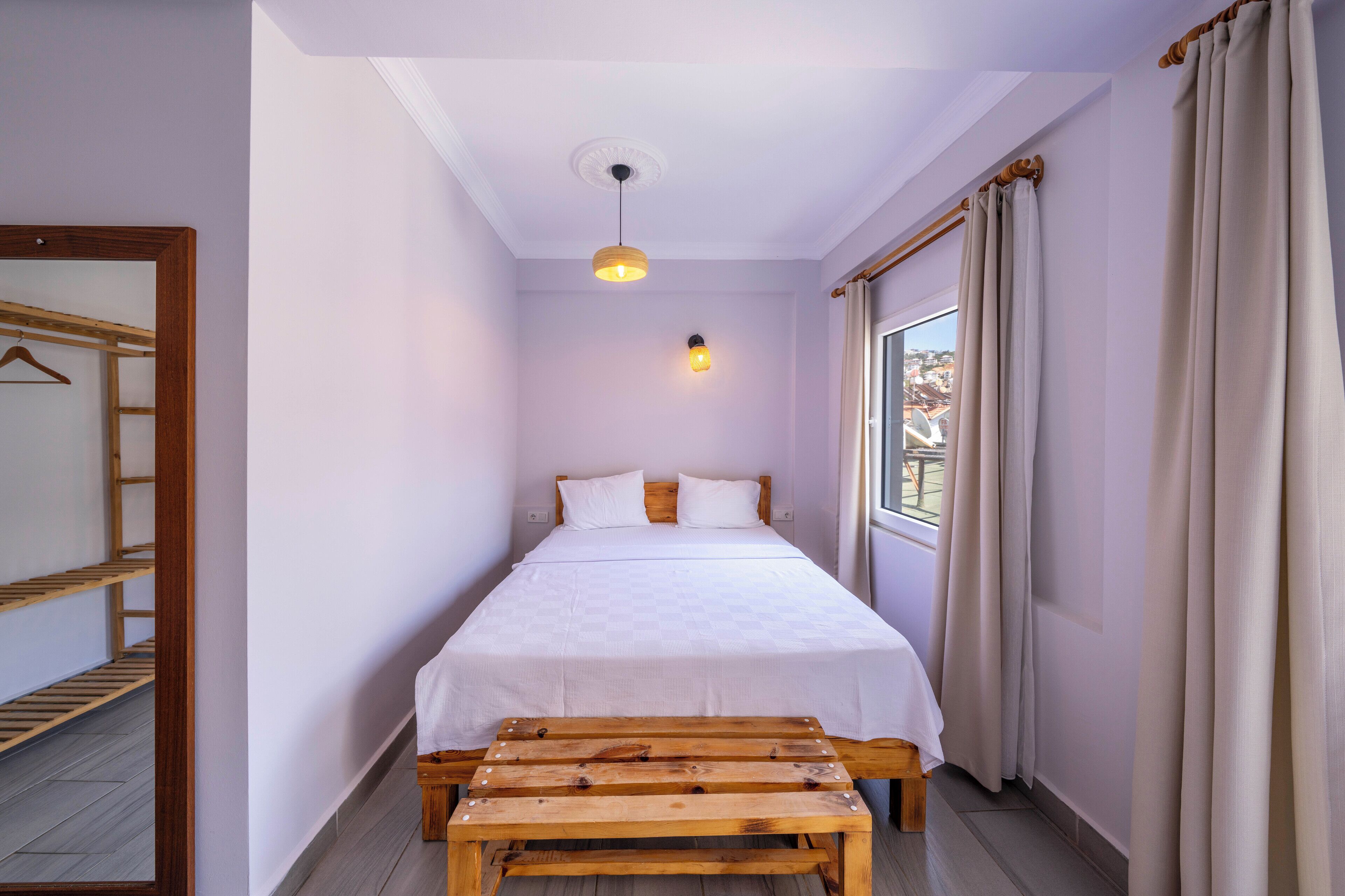 A bedroom with a bed, a wooden bench, a hanging light fixture, and a window with curtains.