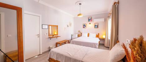 Quarto de hotel com duas camas, um banco de madeira, uma mesinha e um espelho.