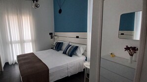 Une chambre d’hôtel avec un lit, une table de chevet, un miroir et une fenêtre avec des rideaux.