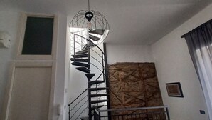 Un escalier en colimaçon doté d’un design original en forme de structure filaire, un mur à texture et une fenêtre avec des rideaux.