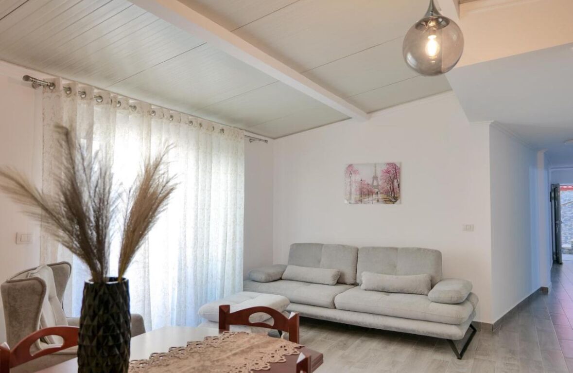 A living room with a sofa, a dining table with chairs, a vase with dried plants, and a painting on the wall.