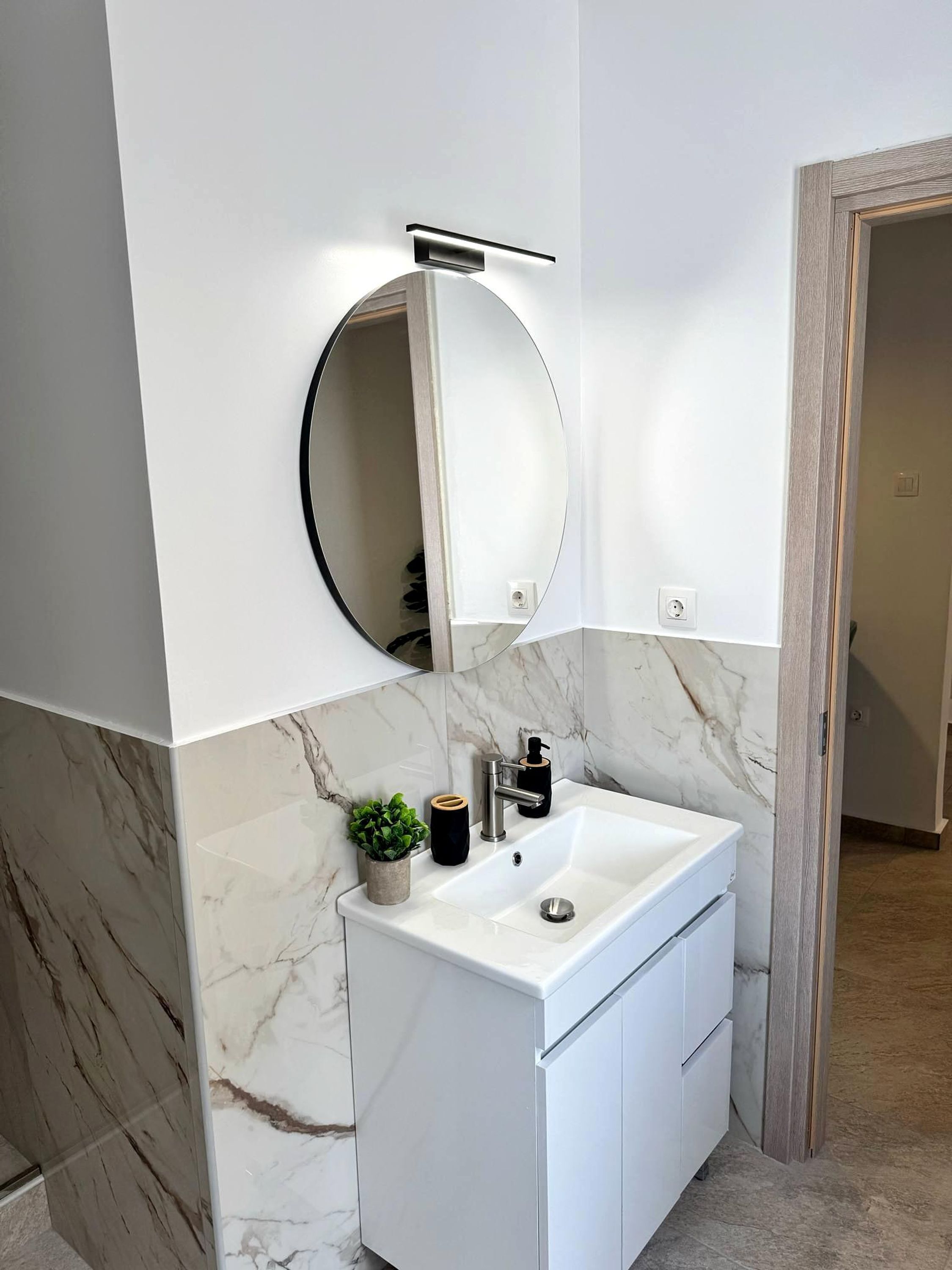 A modern bathroom with a white vanity, a round mirror, and a marble backsplash.