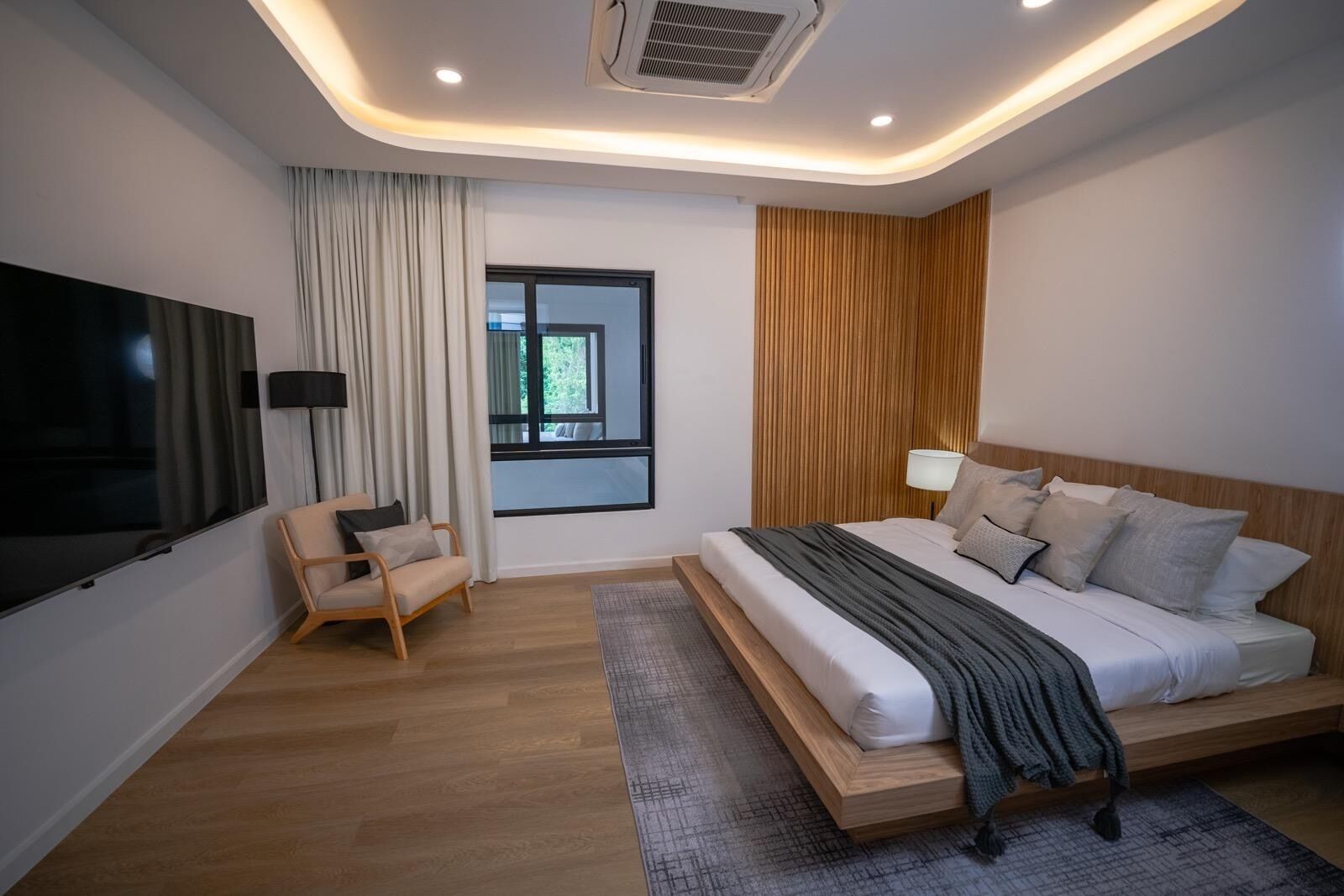 A modern bedroom with a large bed, a chair, a TV, and a window.