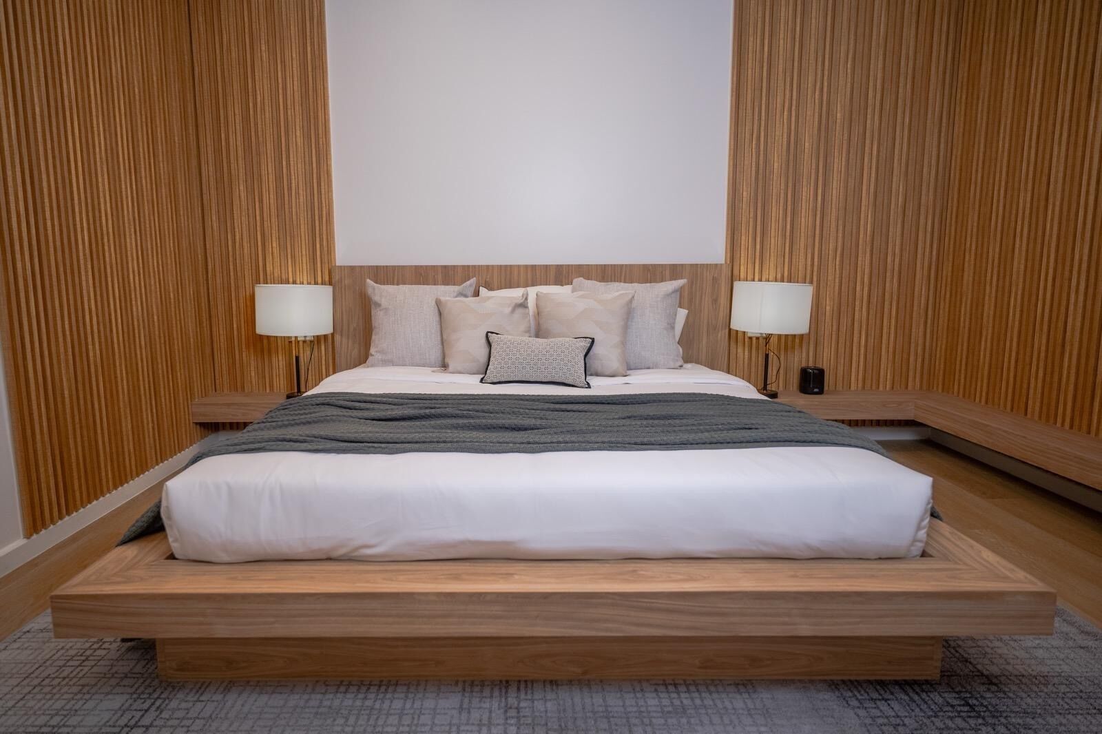A modern bedroom with a large bed, wooden headboard, and two bedside lamps.