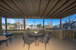 A covered outdoor patio with a table and chairs, a hanging wind chime, and a view of houses and trees.