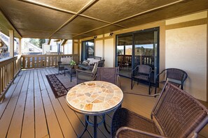A covered outdoor patio with wicker furniture, a stone-tiled table, and a view through glass doors.