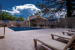 A swimming pool with lounge chairs and umbrellas, surrounded by a fenced area with tables and chairs.