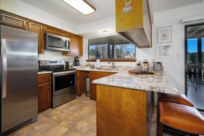 A kitchen with a stainless steel refrigerator, microwave, stove, and oven, wooden cabinets, a granite countertop, and a window with blinds.