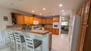 A spacious kitchen with wooden cabinets, a central island with bar stools, a refrigerator, and a microwave. - Spacious home in the heart of Emmett (Emmett)