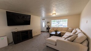 A living room with a large flat-screen TV, a dark entertainment unit, a beige sofa, and a coffee table. - Spacious home in the heart of Emmett (Emmett)