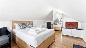 A modern hotel room with a wooden bed, a desk, a chair, and a 'GUEST READY' sign.