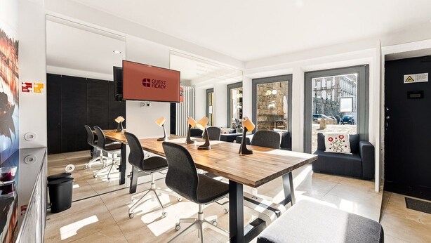 A modern conference room with a wooden table, black chairs, and a large screen.