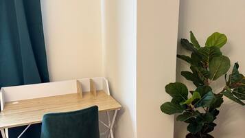A corner room with a wooden herringbone floor, a white desk with a green chair, a potted plant, and a blue curtain.