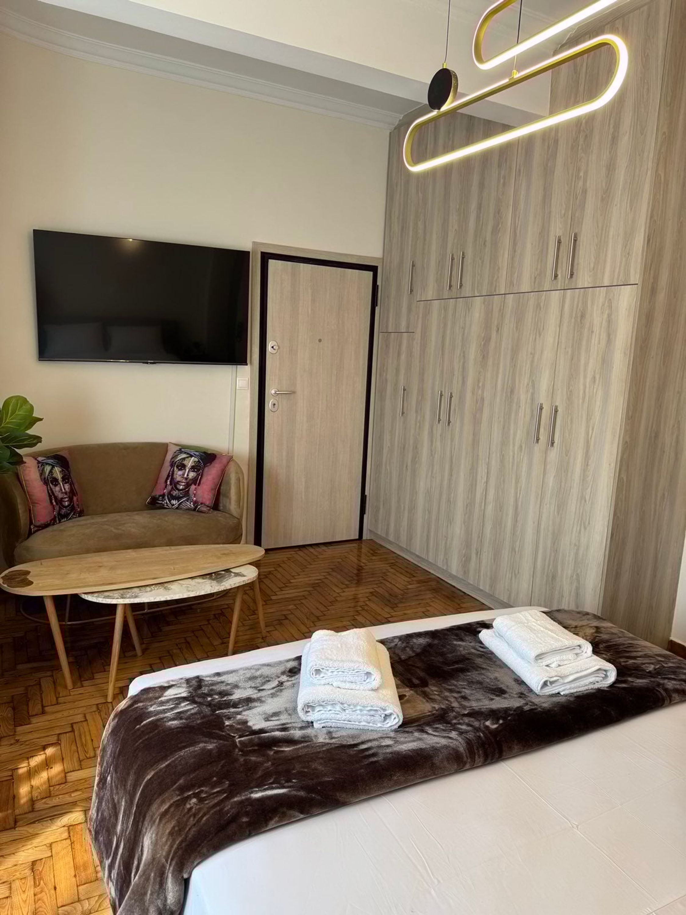 A modern hotel room with a bed, a sofa, a TV, and a wardrobe.