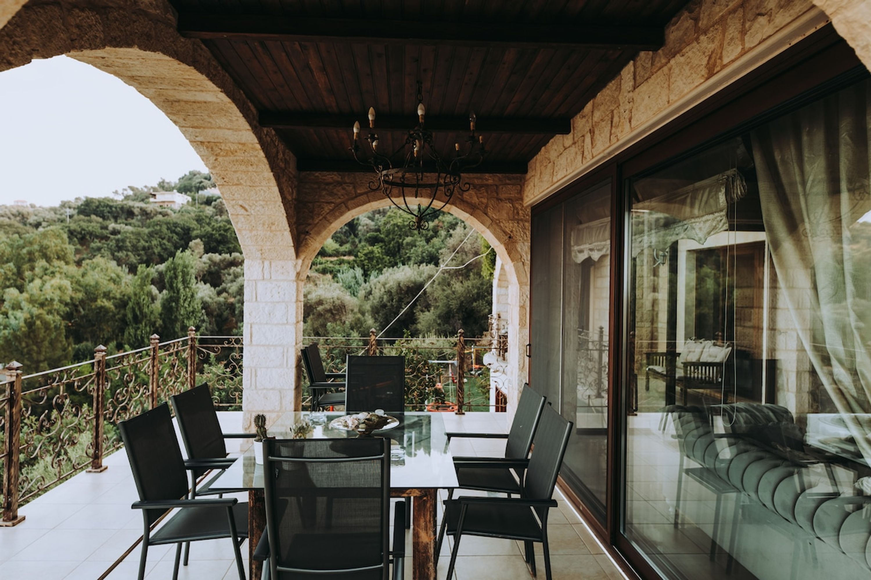 An outdoor patio with a table and chairs, a glass wall, and a view of the surrounding landscape.