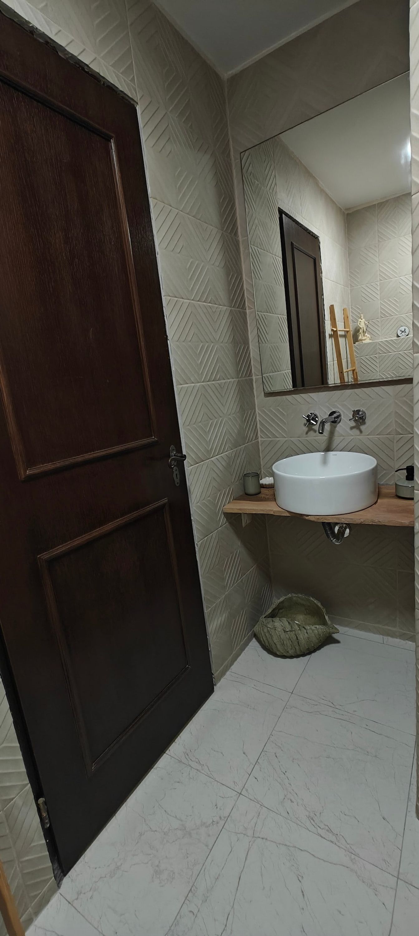 A bathroom with a wooden door, a white sink, a mirror, and patterned walls.