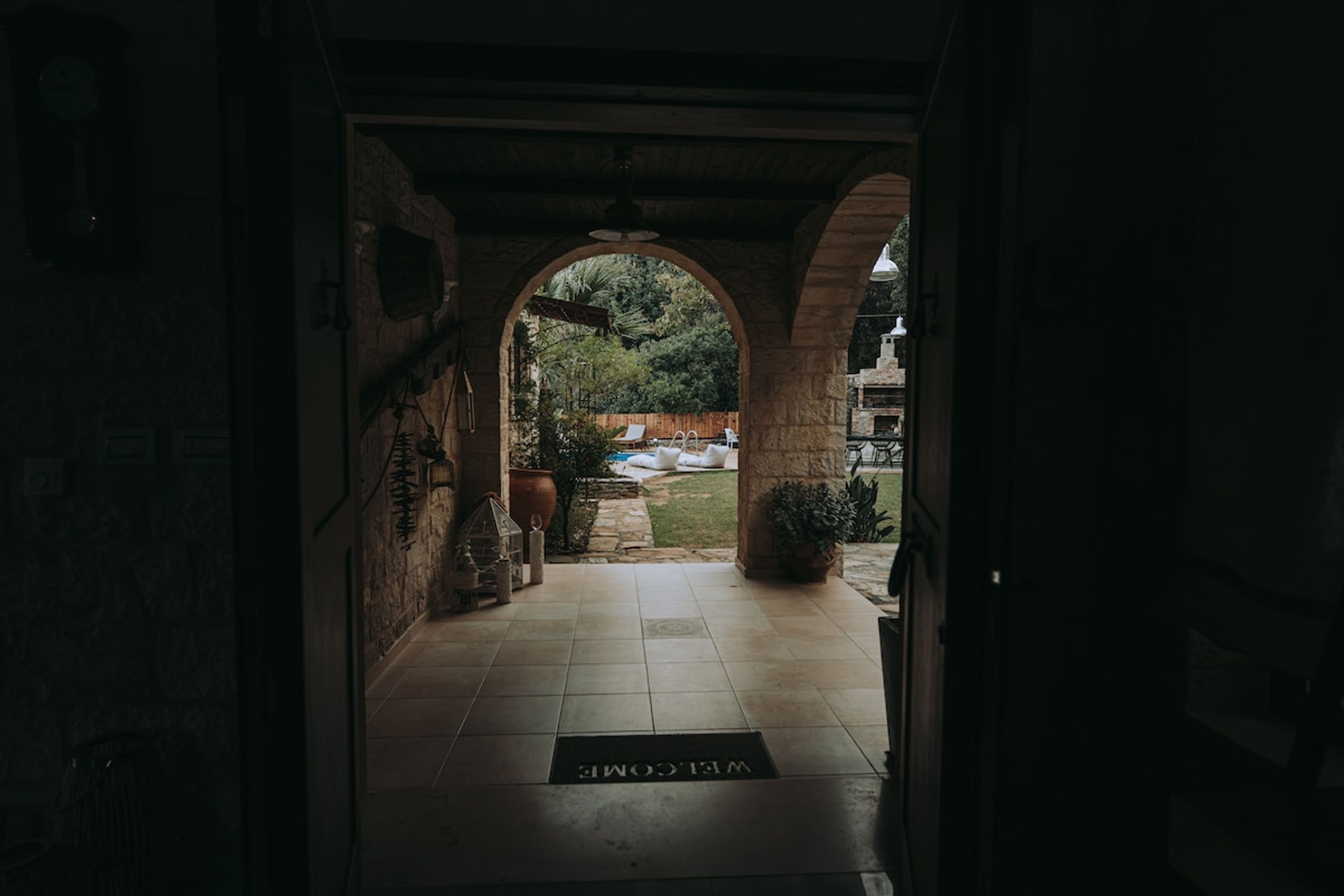 An arched entrance with a welcome mat, stone walls, and a view of a garden.