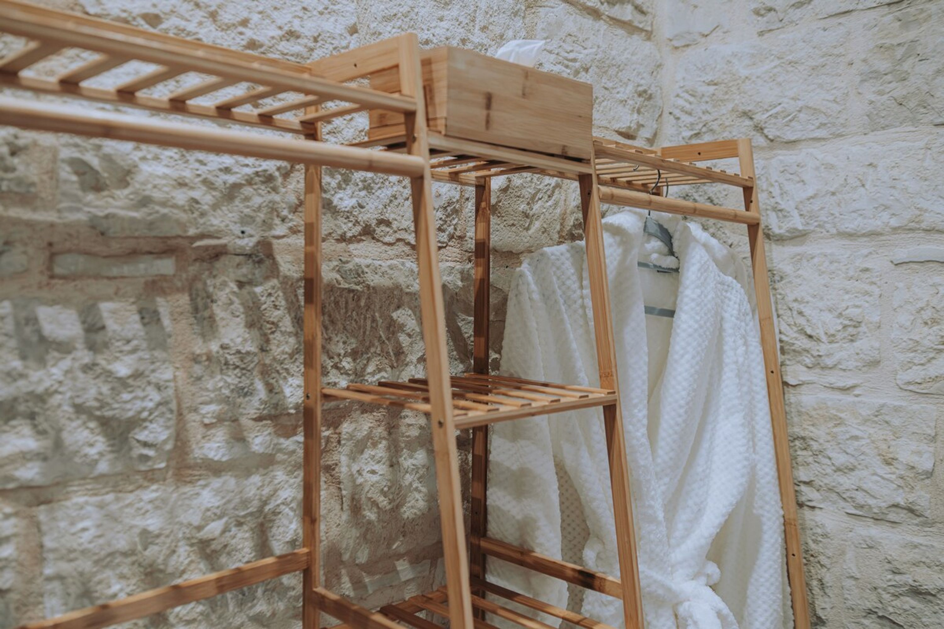 A wooden drying rack with a white towel hanging on it, set against a textured stone wall.